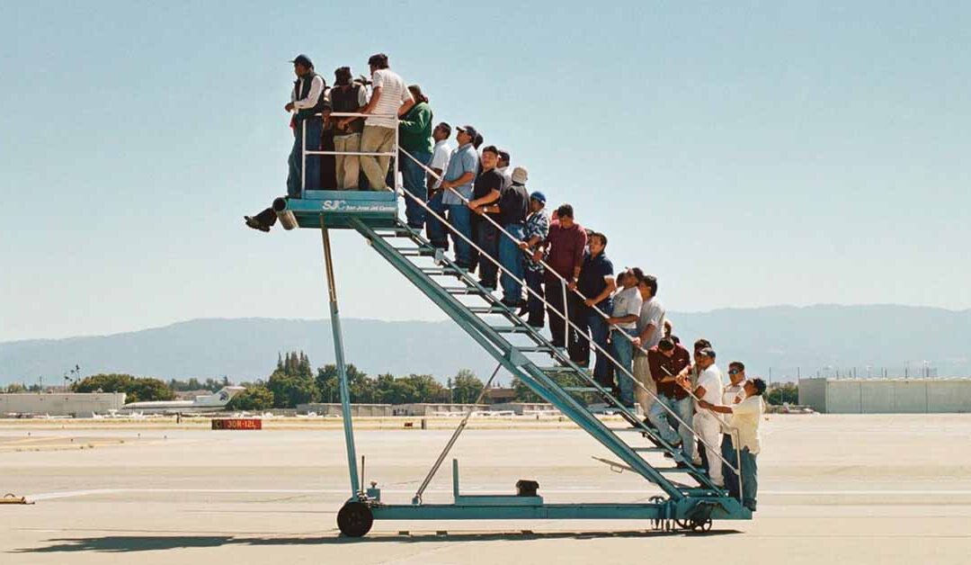 El silencioso exilio de los chilenos - La obra de Adrian Paci retrata a un grupo de personas de pie sobre una escalerilla móvil de avión que no lleva a ninguna parte, simbolizando la condición suspendida de los migrantes y la espera interminable en la frontera de refugiados.